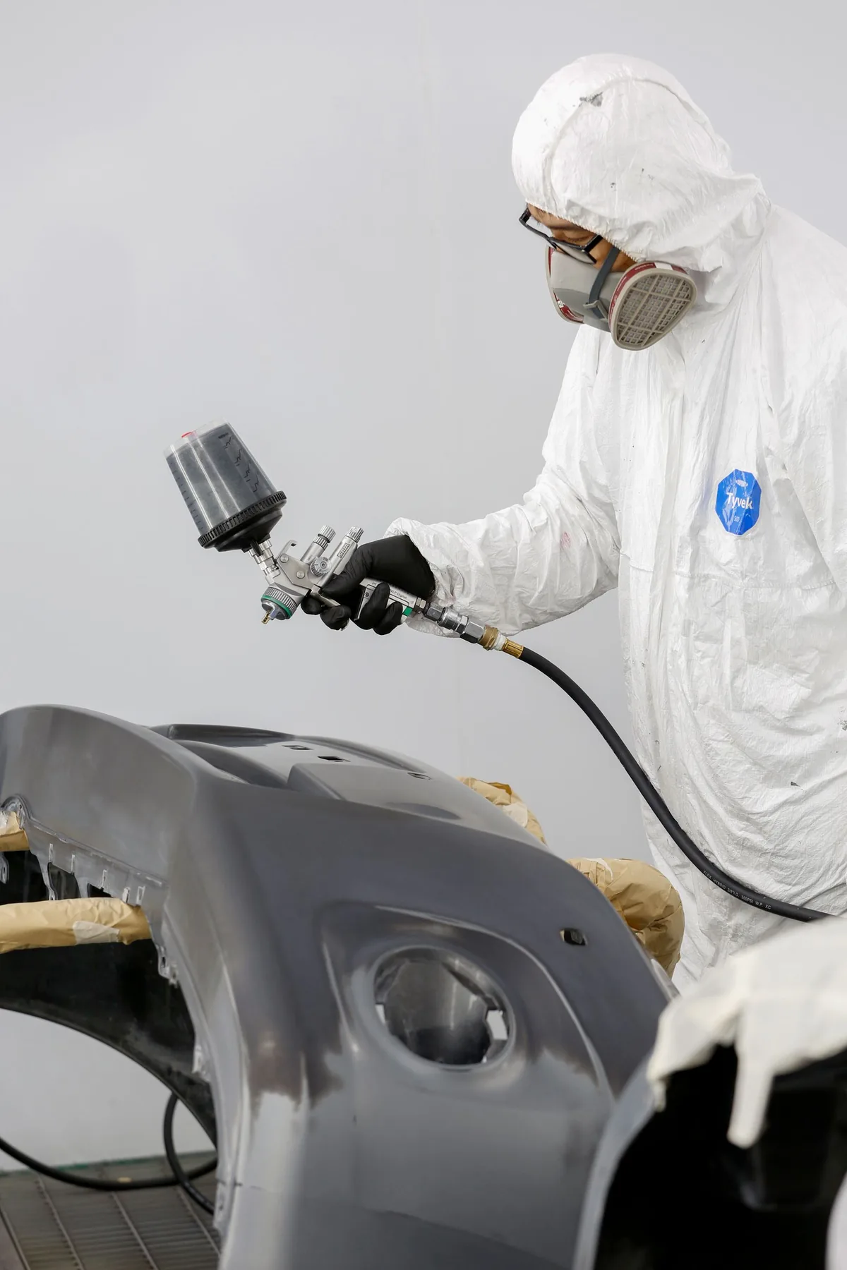 Stock photograph of a technician spray painting a detached bumper in protective clothing
